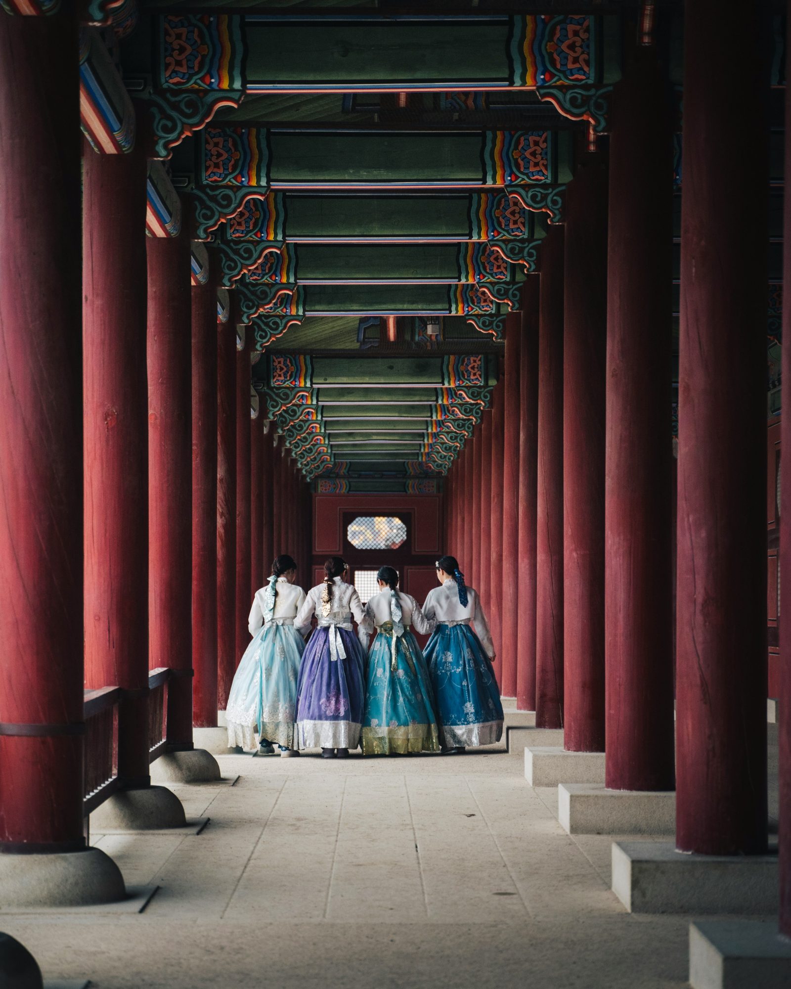 Women in hanbok walking through a red palace corridor in Seoul